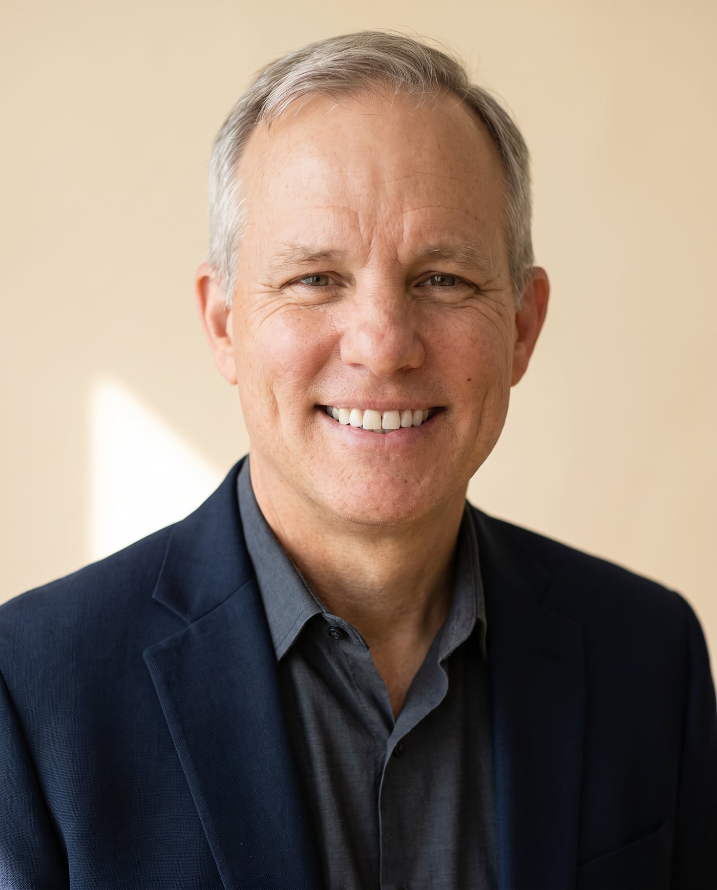 Portrait of Jerry Lee, co-founder of Klauve, smiling in a navy blazer against a warm cream wall.
