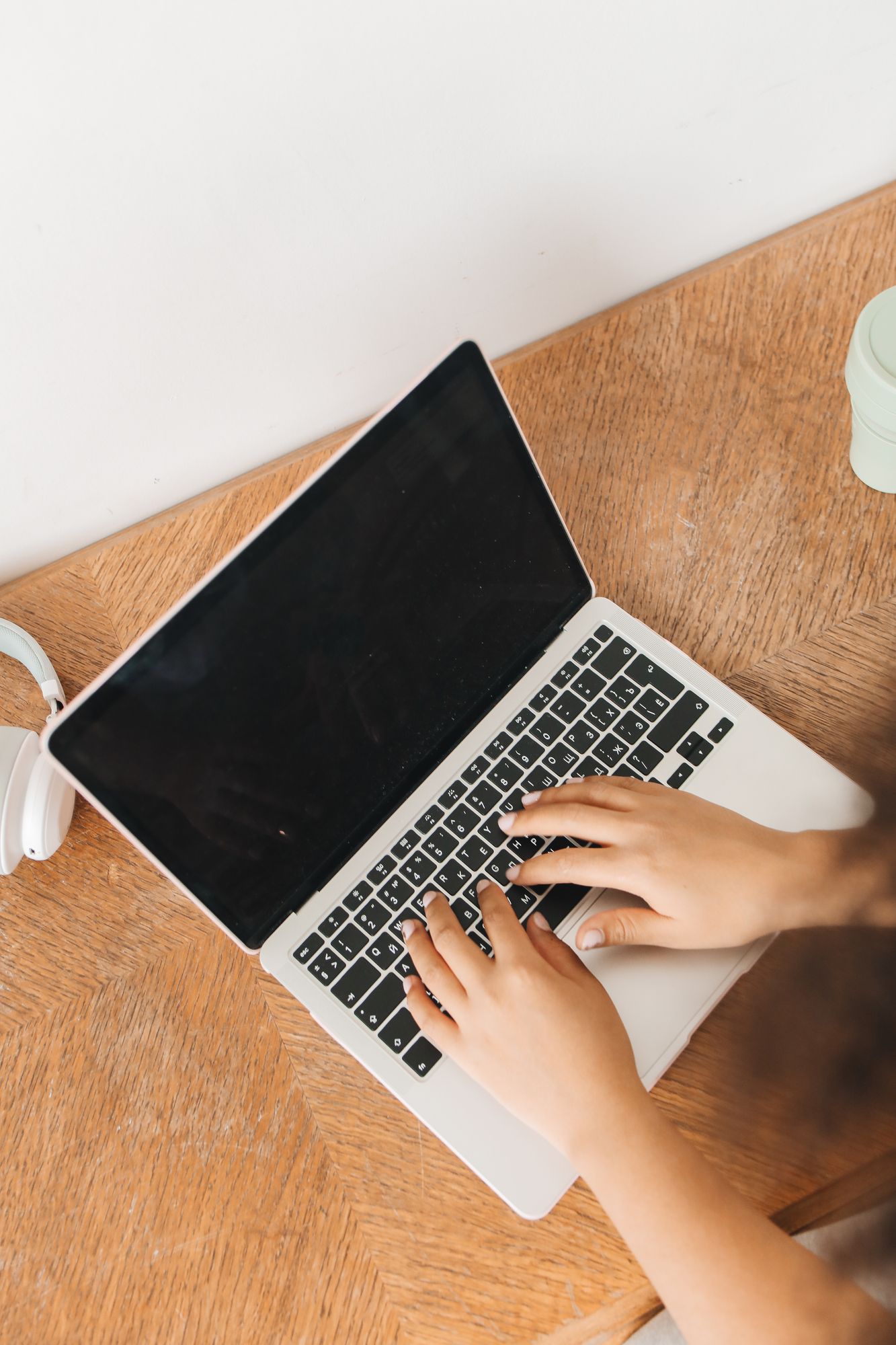 Overhead view of a pair of hands typing on a laptop on a warm wooden table.